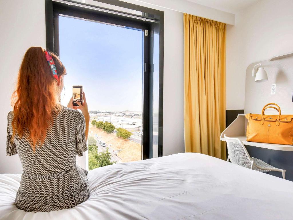 鲁瓦西昂法兰西宜必思尚品巴黎戴高乐机场酒店的一位女士拍着卧室窗户的照片