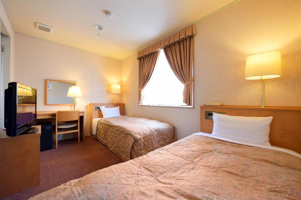 山形市Hotel Capital in Yamagata的酒店客房设有两张床、一张桌子和一台电视。
