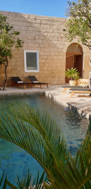ŻabbarPalazzo Pisani Malta B&B的一座带两把躺椅的游泳池以及一座建筑