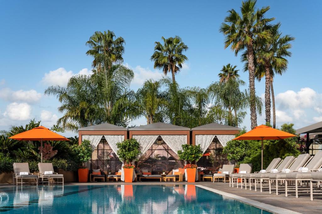 洛杉矶洛杉矶比佛利山庄四季酒店的一个带椅子和遮阳伞及棕榈树的度假游泳池