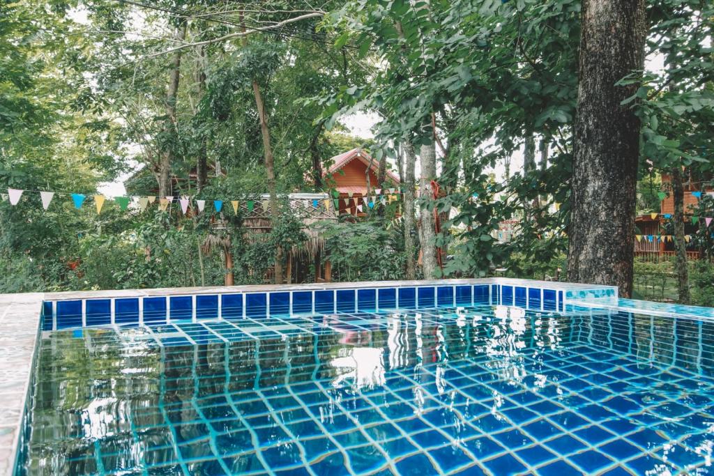 彭世洛Akchanok Homestay的蓝色瓷砖游泳池,后面有树木