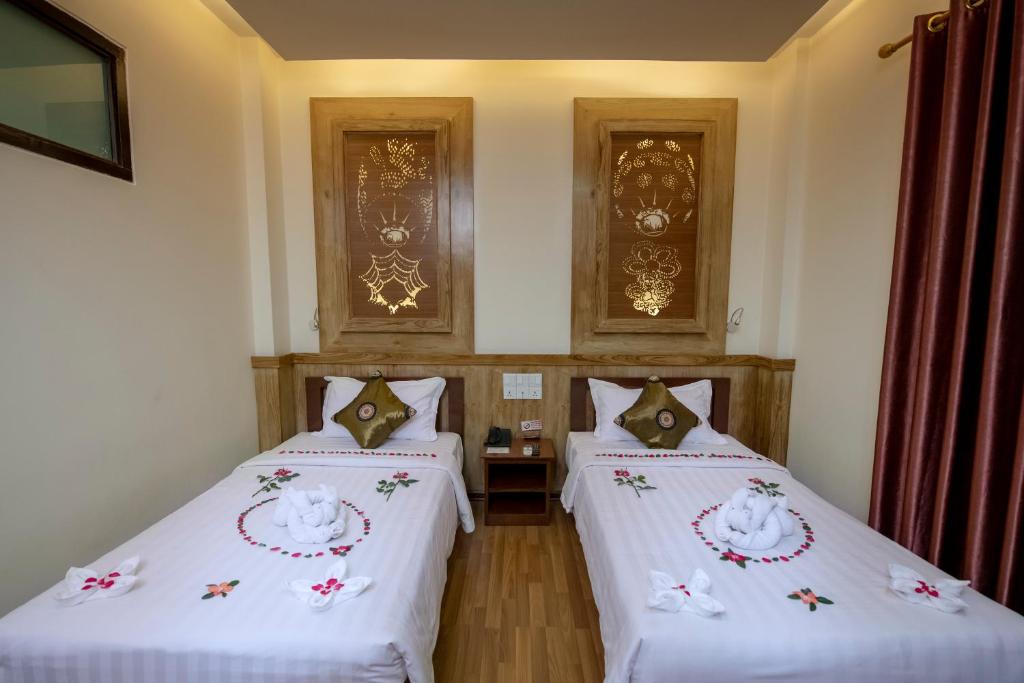 东枝UCT Taunggyi Hotel的客房内的两张床,配有白色床单和鲜花