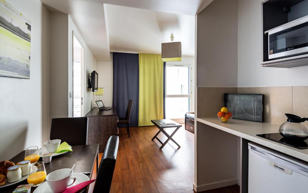 布洛涅-比扬古Lagrange Apart’Hotel Paris-Boulogne的厨房以及带桌椅的起居室。