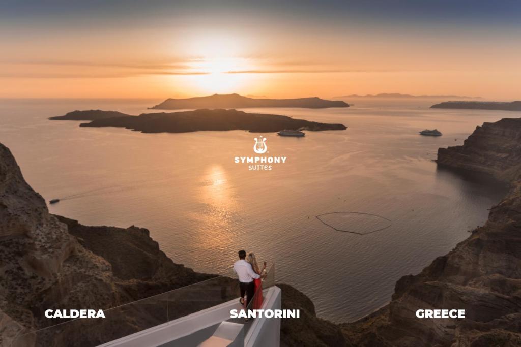 皮尔戈斯Symphony Suites Santorini的一对夫妇站在悬崖边,望着大海