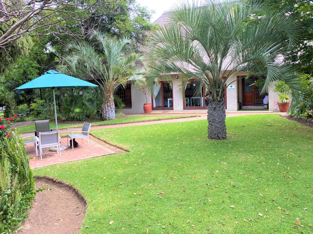肯普顿帕克Safari Club Guest Lodge OR Tambo International Airport的花园设有两把椅子、一张桌子和一把遮阳伞