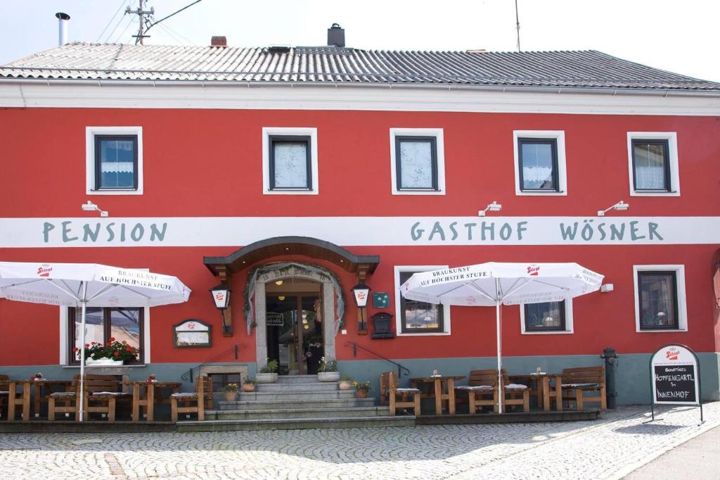 MünzkirchenGasthof Wösner的一座红色的建筑,前面设有桌子和遮阳伞