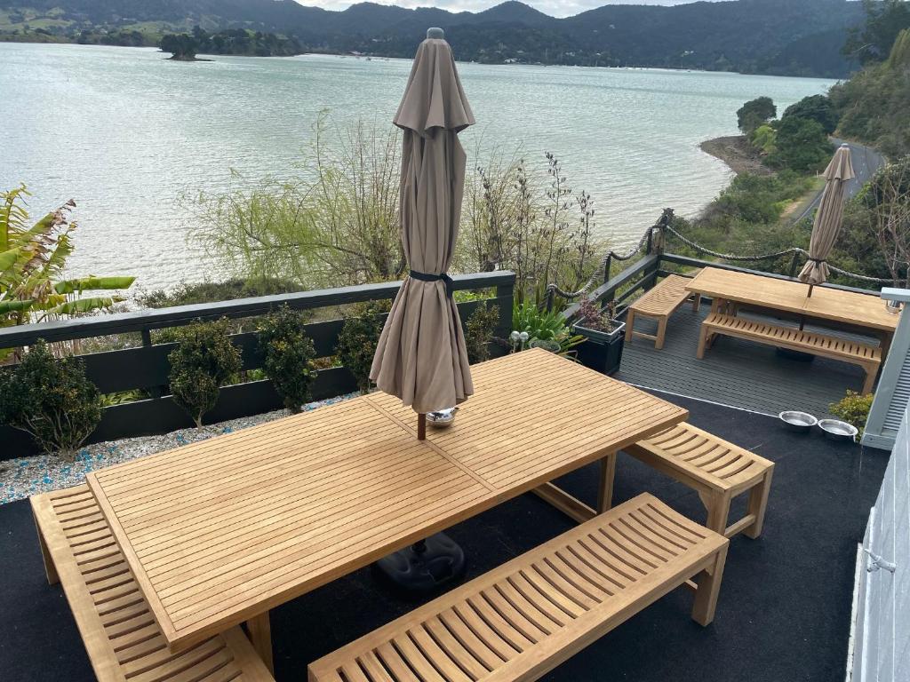 WhangaroaPacific Harbour Lodge的水边甲板上的木桌和遮阳伞