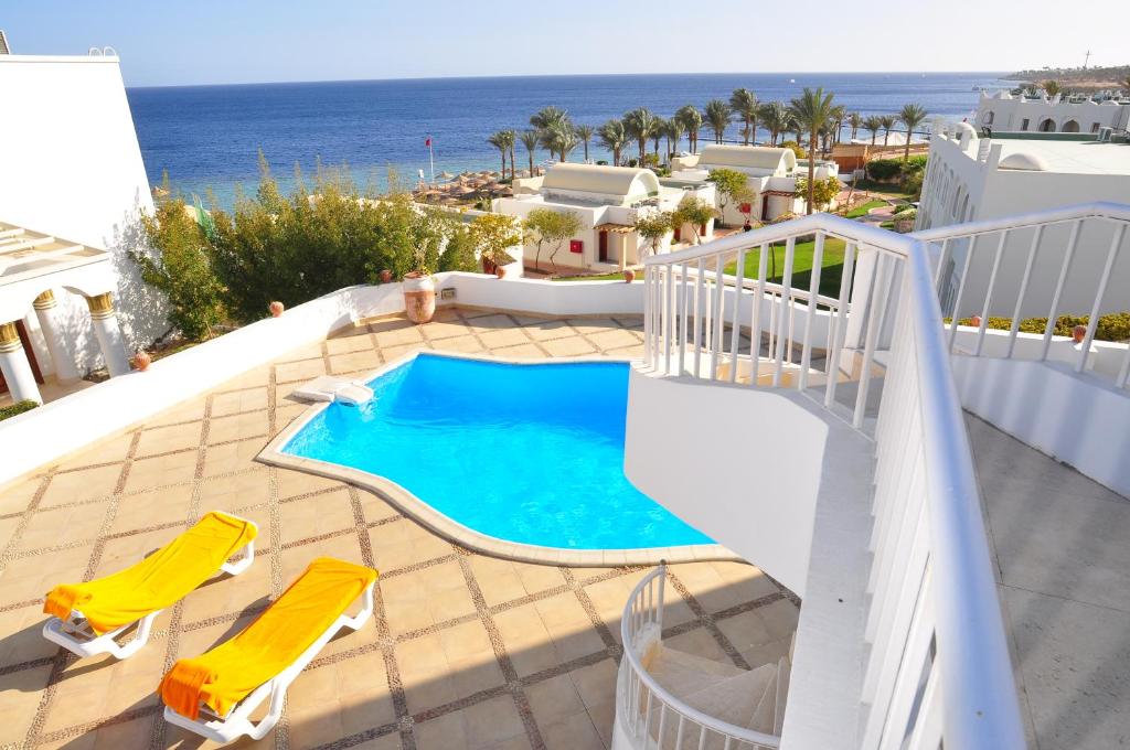 沙姆沙伊赫卡尔顿豪华别墅的享有带两把椅子的游泳池和大海的景致。