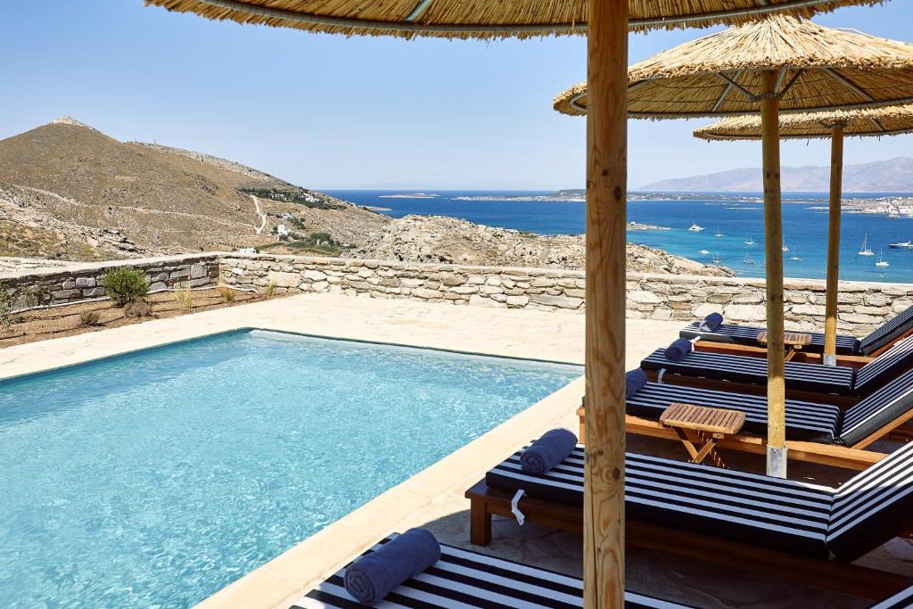 KolympithresAcron Villas Paros的一个带椅子和遮阳伞的游泳池以及大海