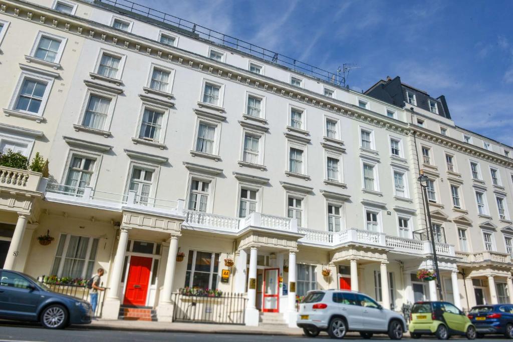 伦敦贝斯特韦斯特日冕酒店的一座白色的大建筑,前面有汽车停放