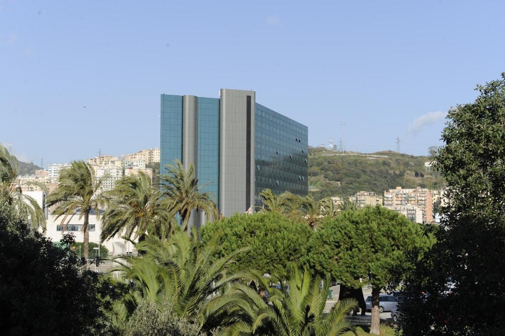 热那亚热那亚塔机场 - 酒店及会议中心的一座高大的建筑,在城市前方有棕榈树