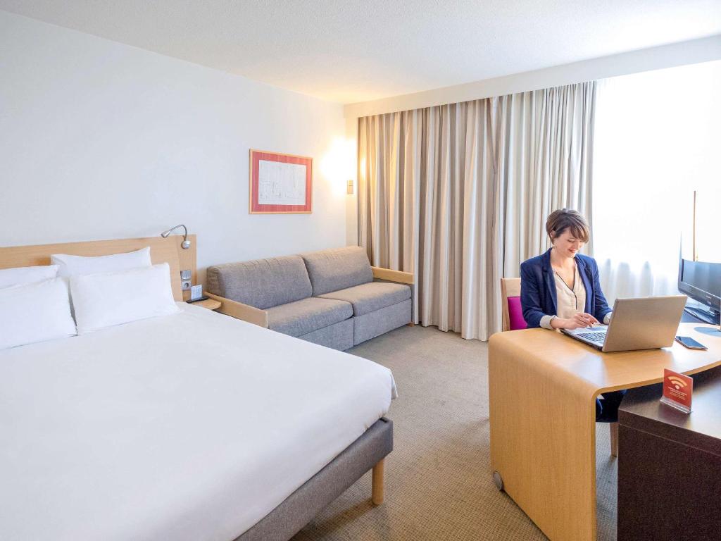 格勒诺布尔格勒诺布尔中央诺富特酒店的坐在酒店房间桌子旁的一位女士,她拿着一台笔记本电脑