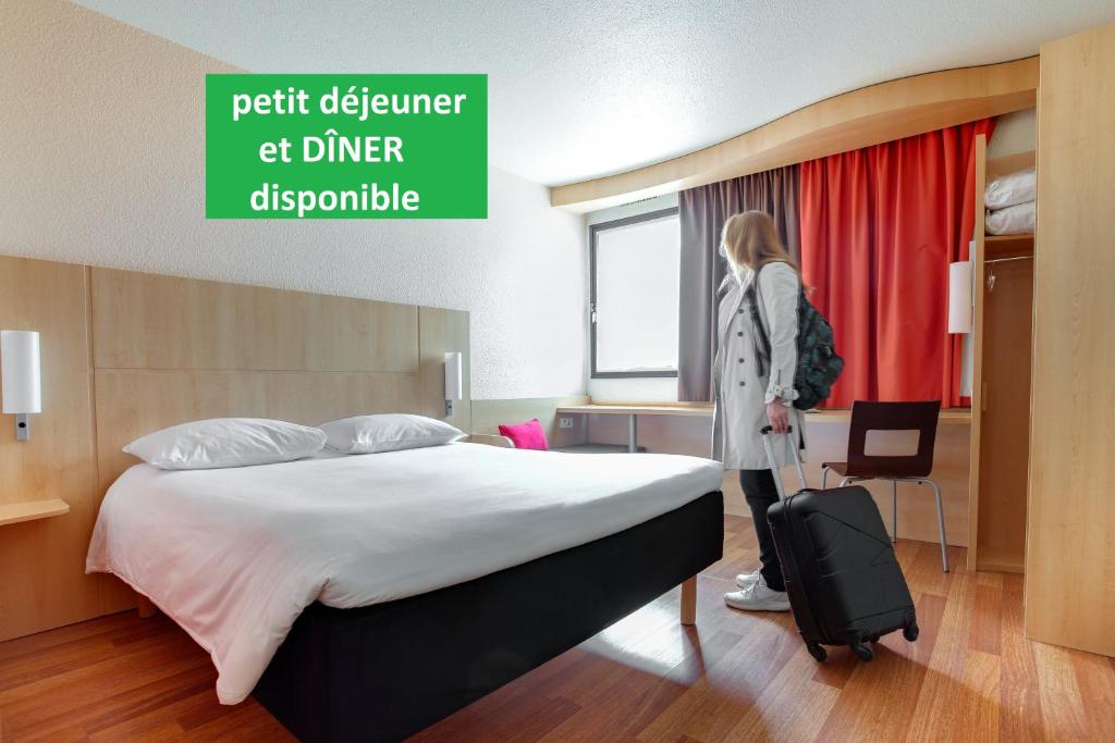 昂热昂热中心酒庄宜必思酒店的一位妇女站在床边,带着手提箱