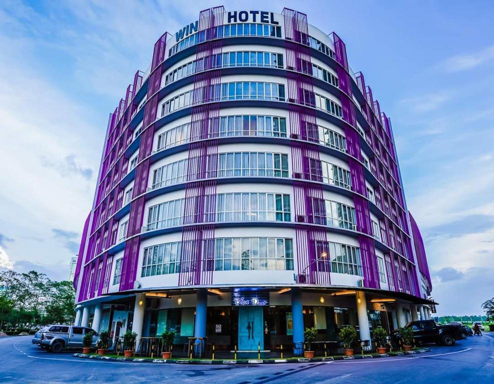 诗巫Win Hotel的一座紫色的酒店大楼,停车场内有车辆停放