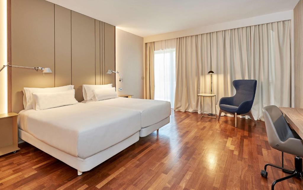 韦尔瓦NH卢斯韦尔瓦酒店的卧室配有一张白色大床和一张蓝色椅子