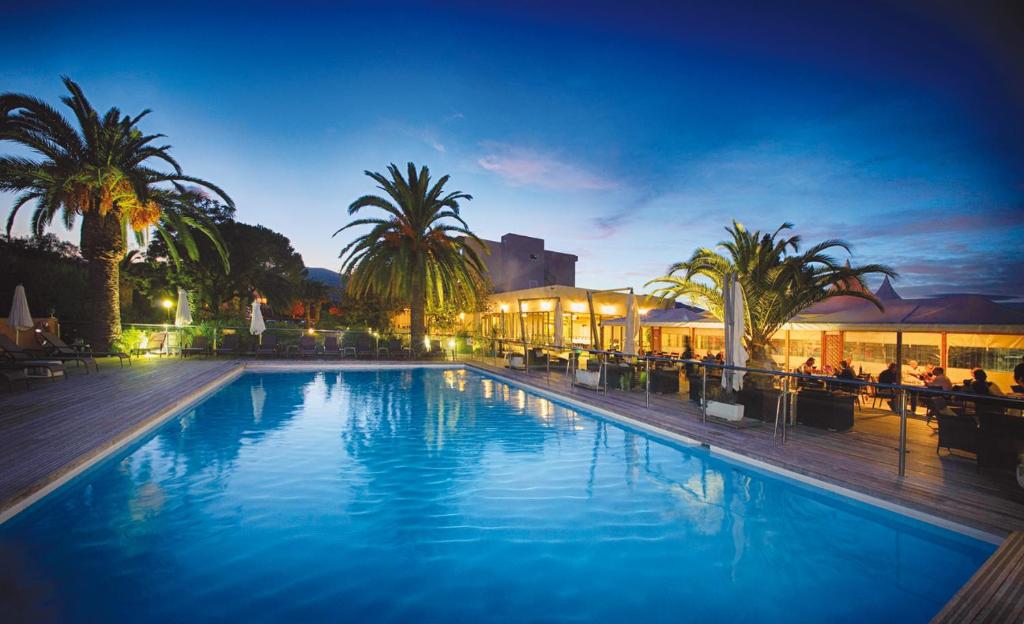 卢恰纳Hôtel Spa Restaurant La Madrague的一座棕榈树大型游泳池和一座建筑