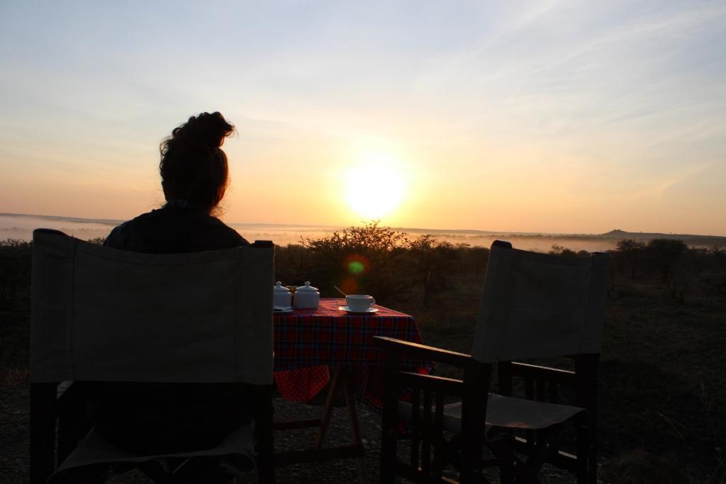 巴纳吉Osero Serengeti Luxury Tented Camp的坐在桌子旁观看日落的女人