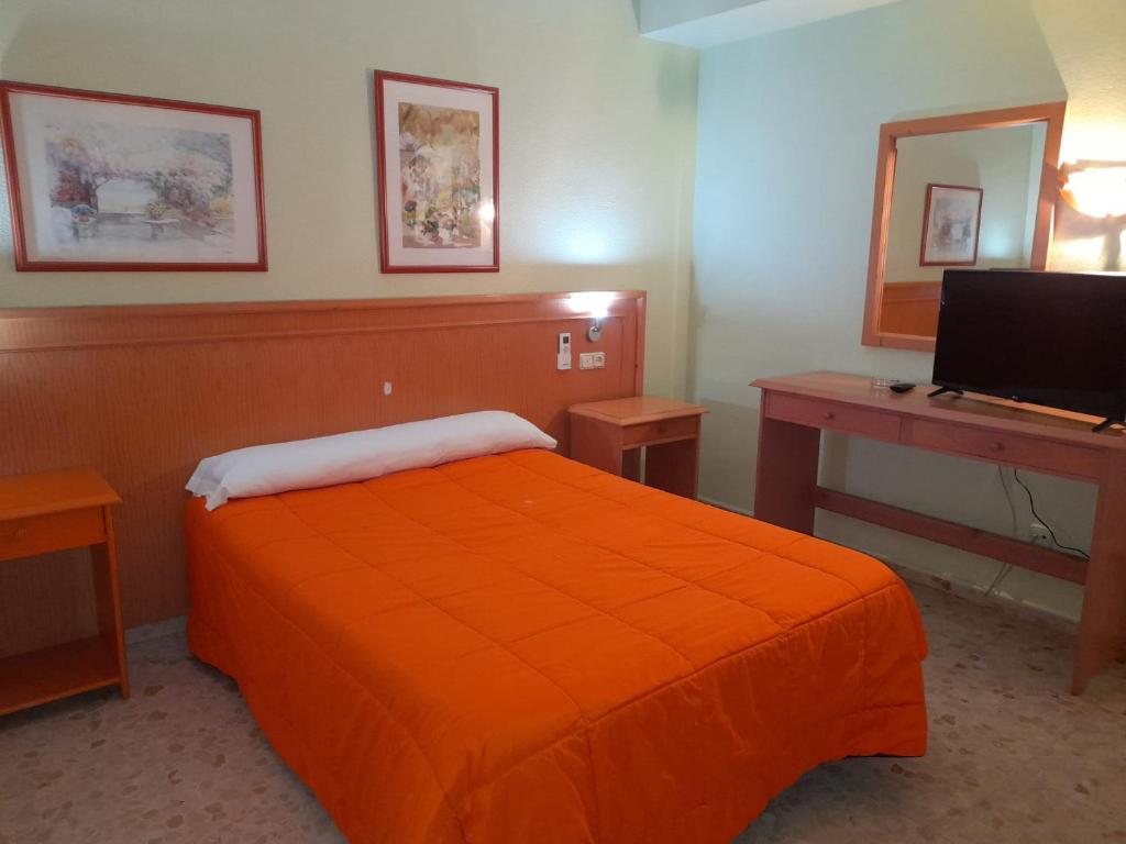 厄尔埃基多Hostal Carlos III的一间卧室配有橙色的床、一张书桌和一台电脑