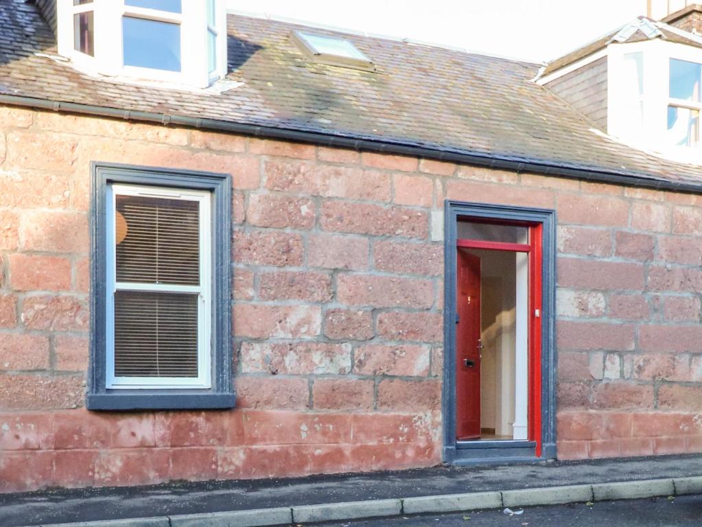 布莱尔高里George Cottage的砖砌建筑,设有两扇窗户和一扇红色的门