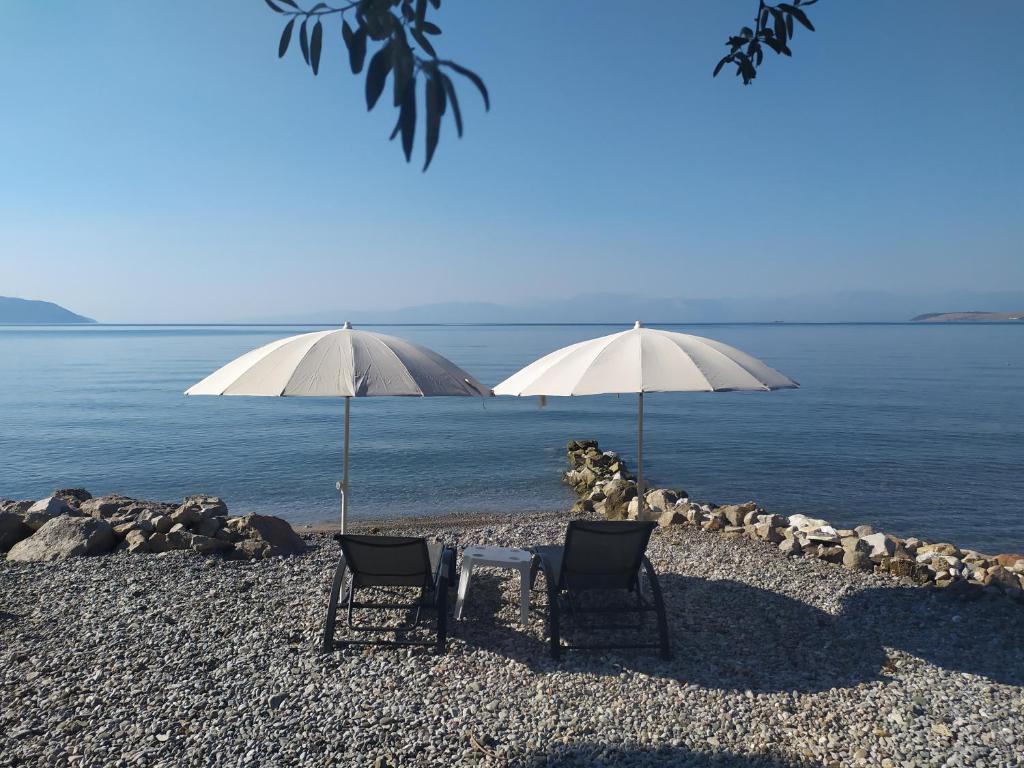 伊泰阿Kalafatis beach home的海滩上的两把椅子、一张桌子和两把遮阳伞