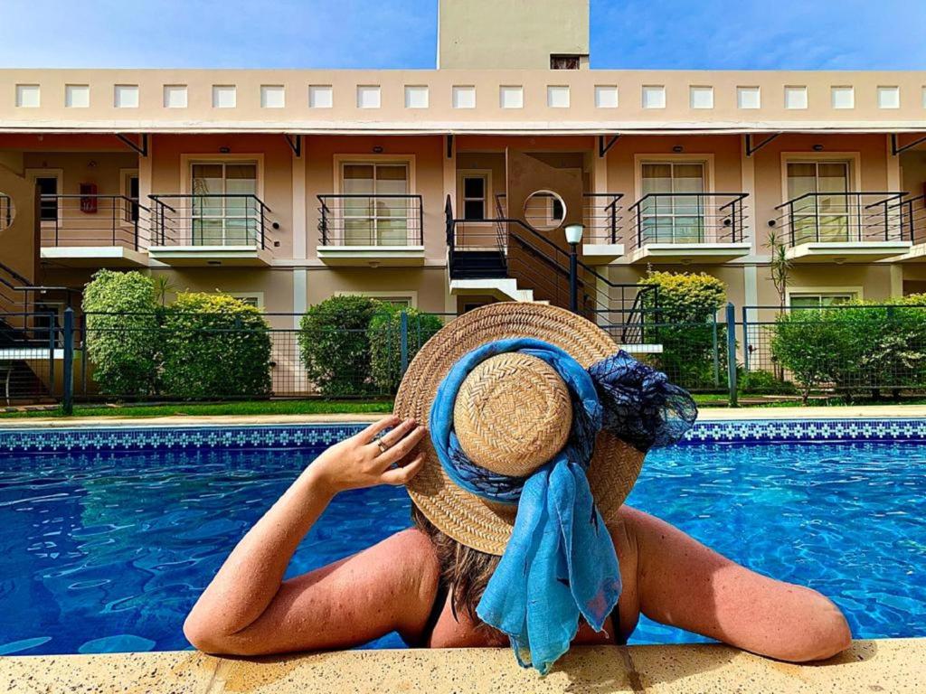 费德拉西翁Mediterraneo Apart Hotel的坐在游泳池旁的戴帽子的女人