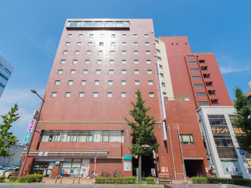 北九州Tabist Hotel Tetora Kitakyushu的一座高大的红砖建筑,前面有一棵树