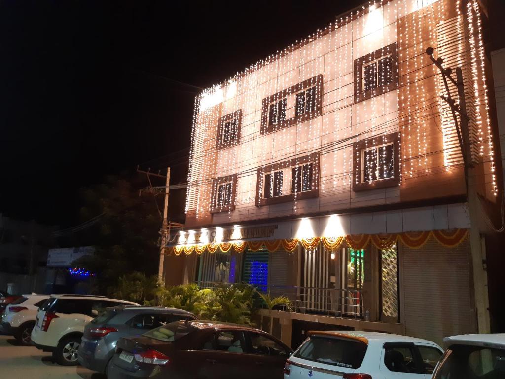 达文盖雷Srigandha Residency "Vaccinated Staff"的一座有照明的建筑,前面有汽车停放