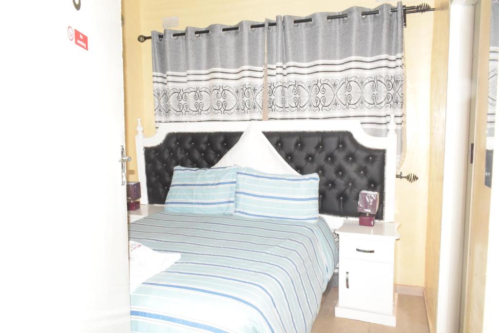 哈拉雷The Crown Inn Guest House的一间卧室配有一张大床和黑色床头板