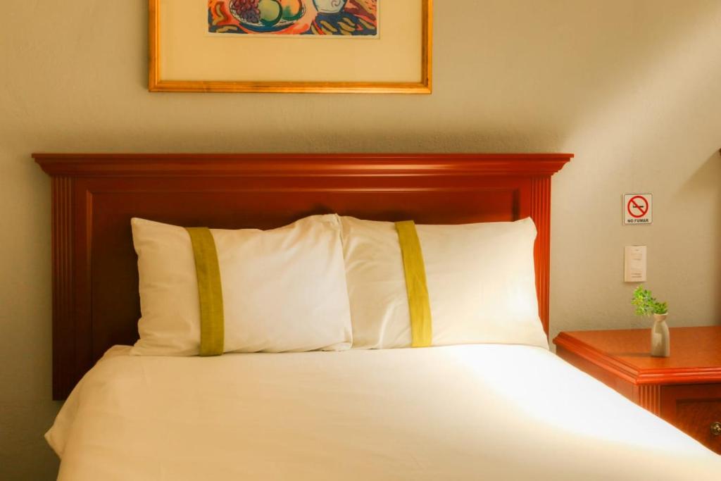 莱昂Suites Bajío的一张带木制床头板和白色枕头的床
