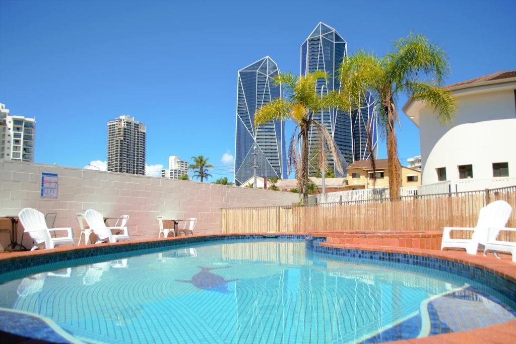 黄金海岸Gold Coast Inn的一座带椅子和棕榈树的游泳池以及建筑