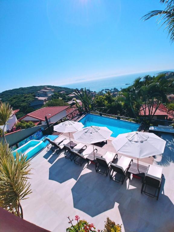 布希奥斯Pousada Vila do Sol的一个带遮阳伞和椅子的游泳池以及大海