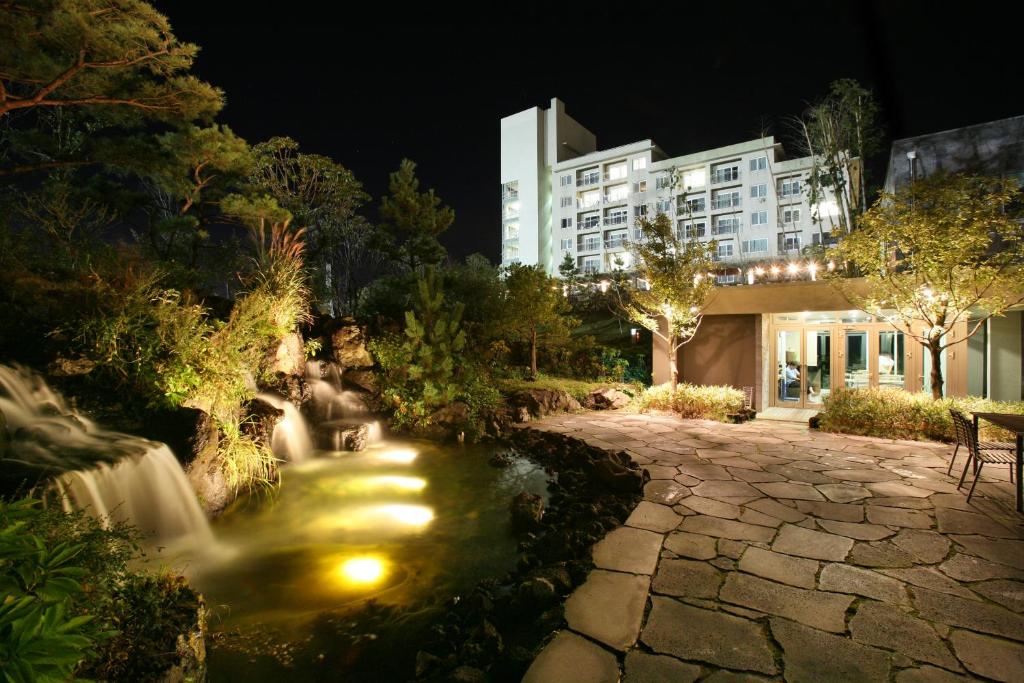 济州市济州韩华度假村的一座带瀑布和建筑的夜间花园