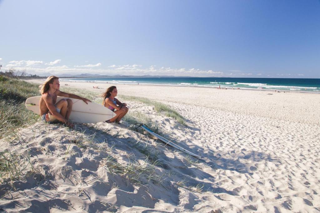 拜伦湾海滩背包客旅馆的两名妇女坐在海滩上,并使用冲浪板