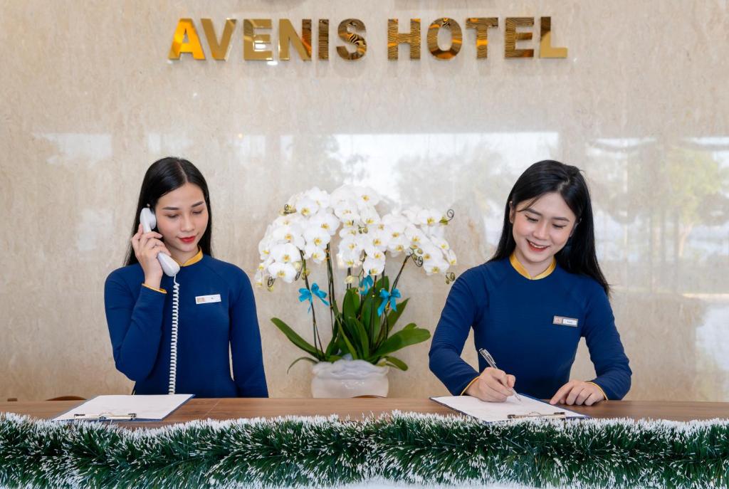 岘港Avenis Hotel的坐在一张桌子上,在手机上说话的两名妇女