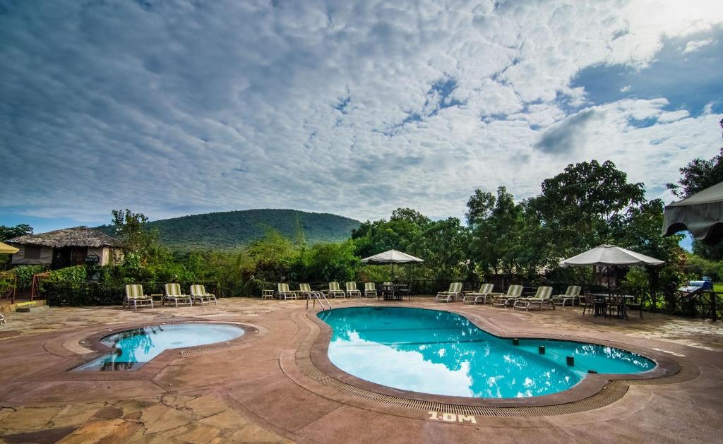 OlolaimutiekSentrim Mara Lodge的一个带桌椅的游泳池以及山脉