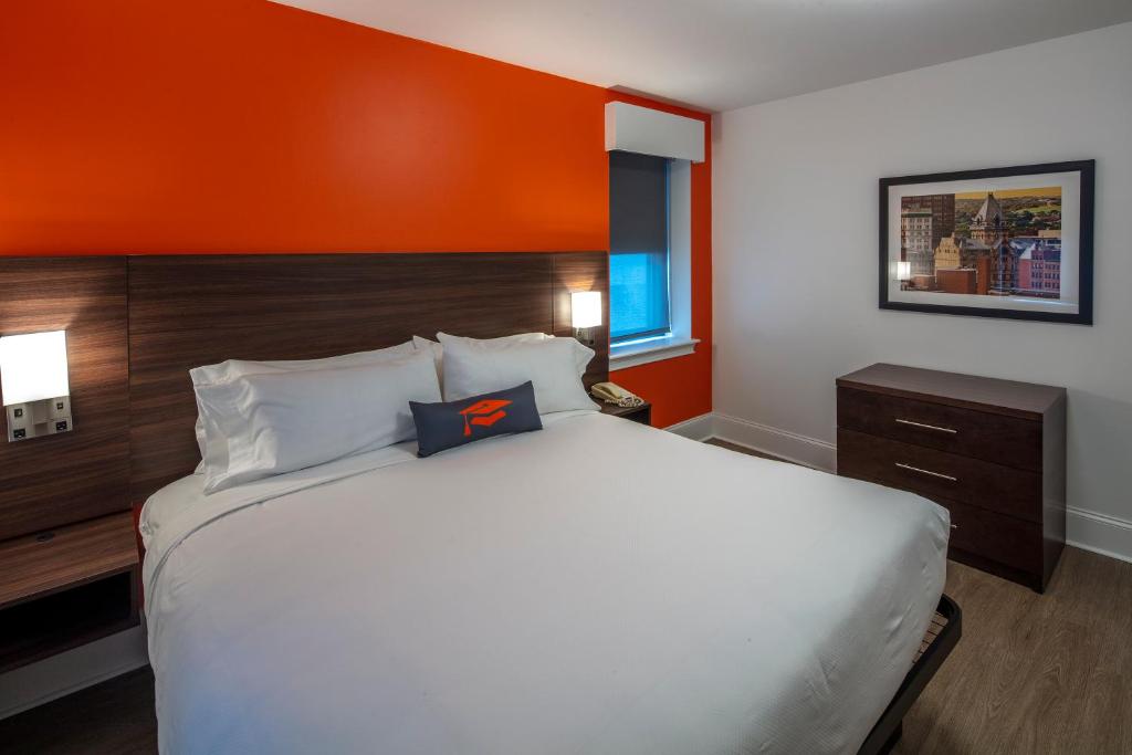 锡拉丘兹Collegian Hotel & Suites, Trademark Collection by Wyndham的一间卧室配有一张带橙色墙壁的大床