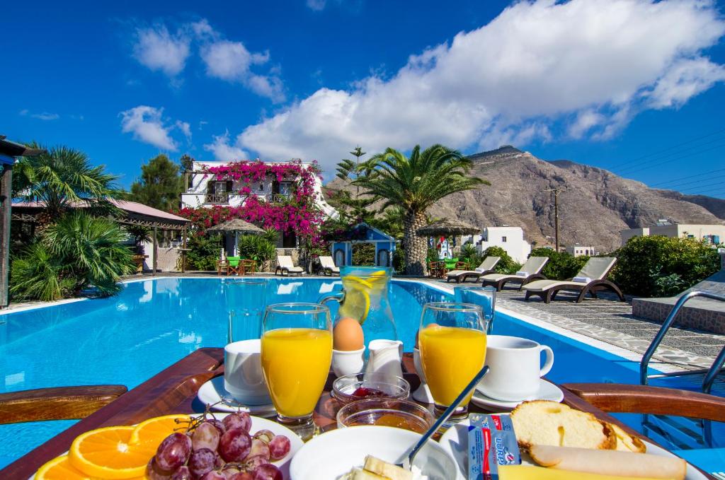 佩里沃罗Holiday Beach Resort Santorini的游泳池旁的餐桌,供应食物和饮料