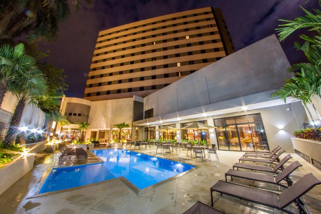 伊瓜苏JL Hotel by Bourbon的酒店游泳池设有椅子,酒店大楼
