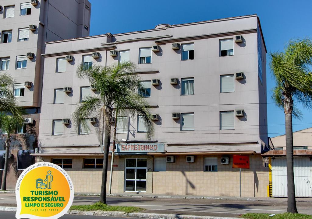 阿雷格里港Hotel Expressinho Aeroporto的一座白色的大建筑,前面有棕榈树