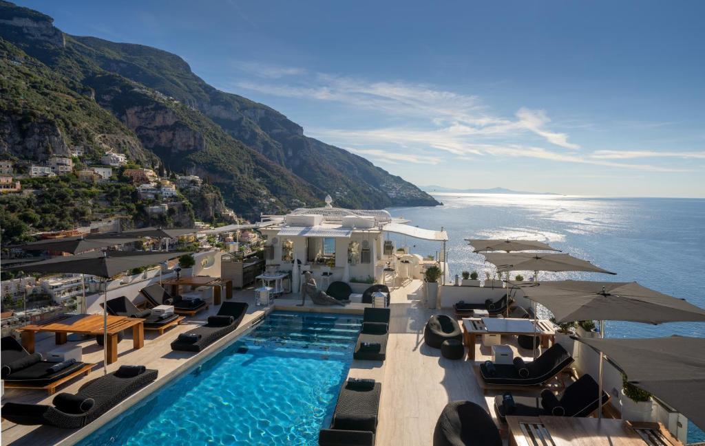 波西塔诺弗兰卡别墅酒店的毗邻大海的带椅子和遮阳伞的游泳池