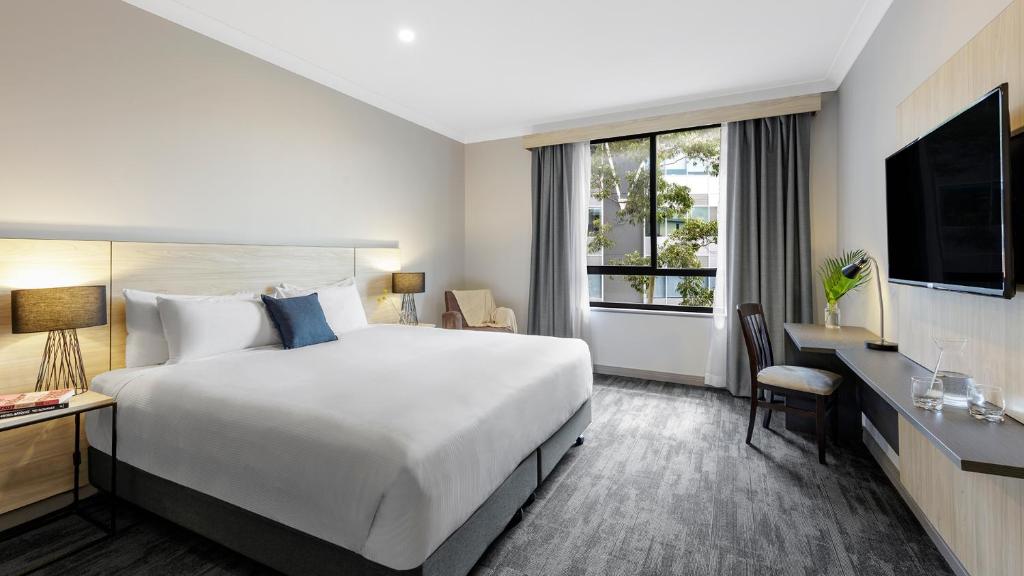 悉尼Oaks Sydney North Ryde Suites的一间设有大床和窗户的酒店客房