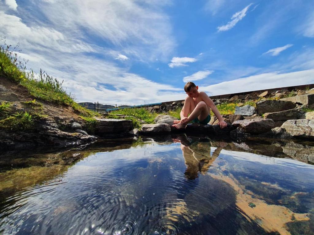 侯尔马维克Hótel Laugarhóll with natural hot spring的坐在水体附近的岩石上的人