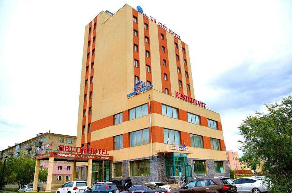 乌兰巴托UB城市酒店的一座高大的建筑,前面有汽车停放