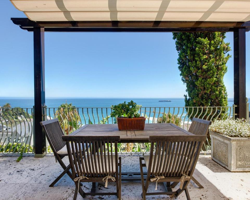 开普敦Villa del Mar - "Luxurious en-suite bedroom with lounge and stunning sea view balcony in Bantry Bay"的一张带椅子的木桌和大海背景