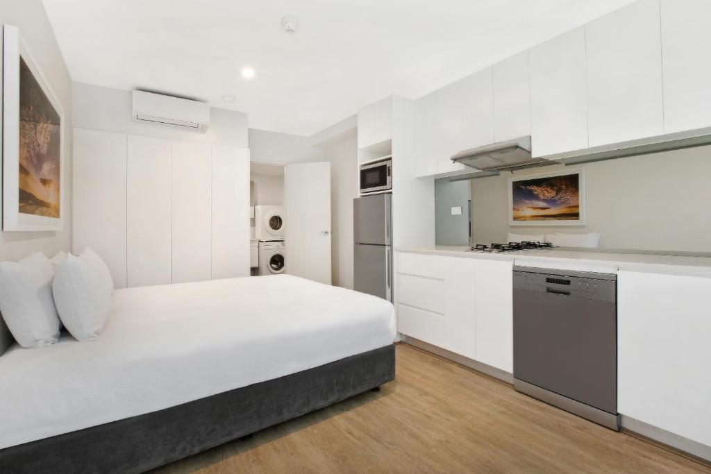 悉尼Bondi Beach Studios Suite的一间白色卧室,配有一张大床和一个厨房