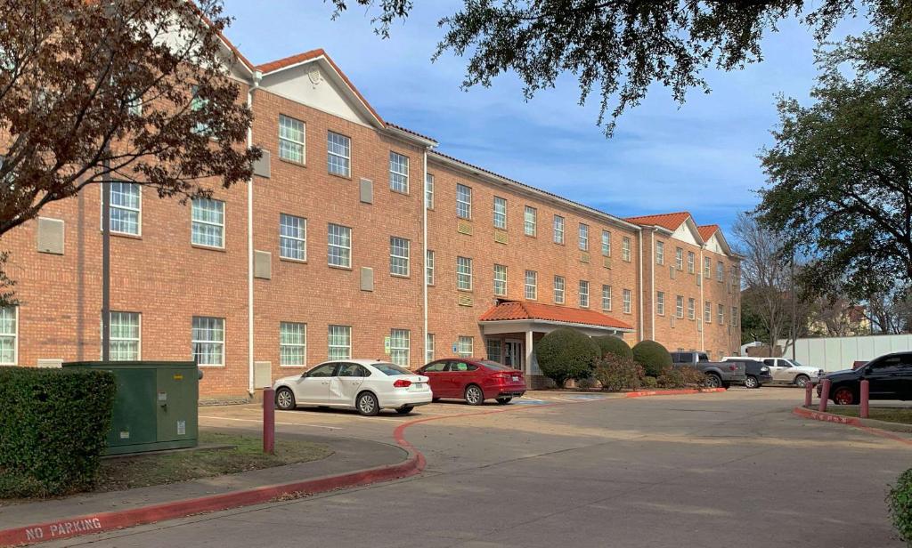 艾迪生MainStay Suites Addison - Dallas的一座大型砖砌建筑,停车场内有车辆停放