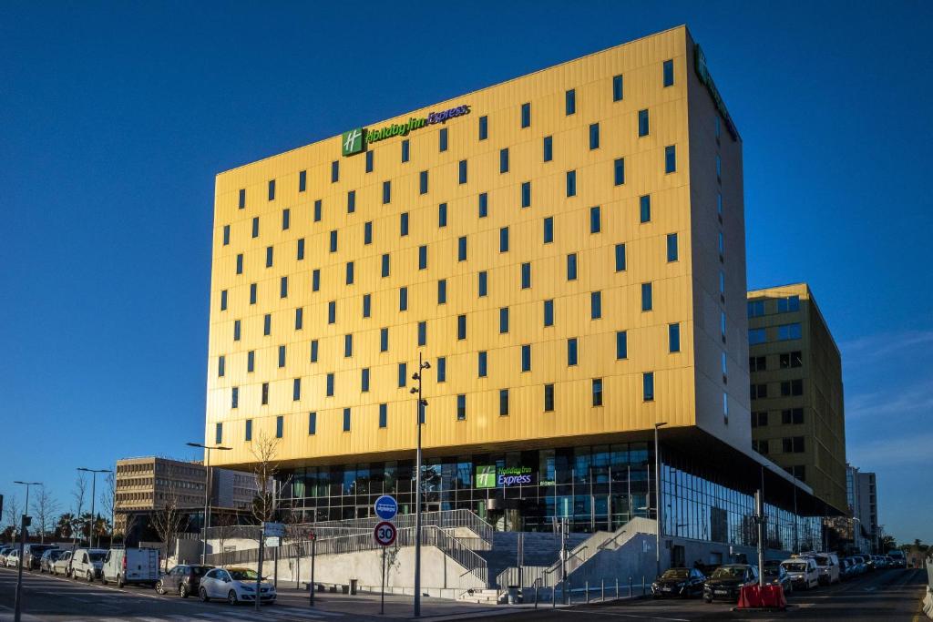 尼斯Holiday Inn Express - Nice - Grand Arenas, an IHG Hotel的一座高大的黄色建筑,前面有汽车停放