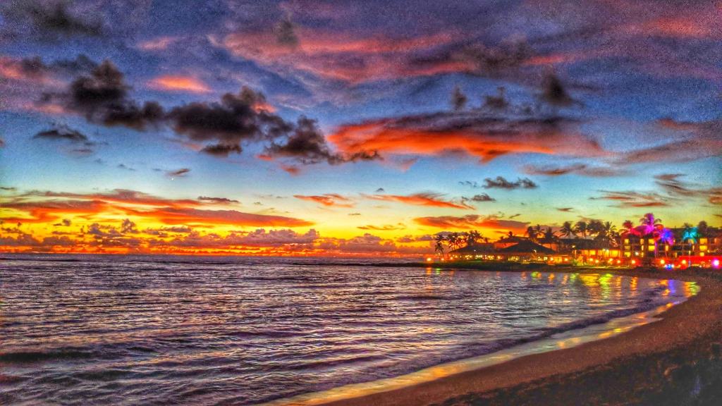 科洛阿ALOHA - Poipu Beach Vacation Condo的海滩上的日落,以城市为背景