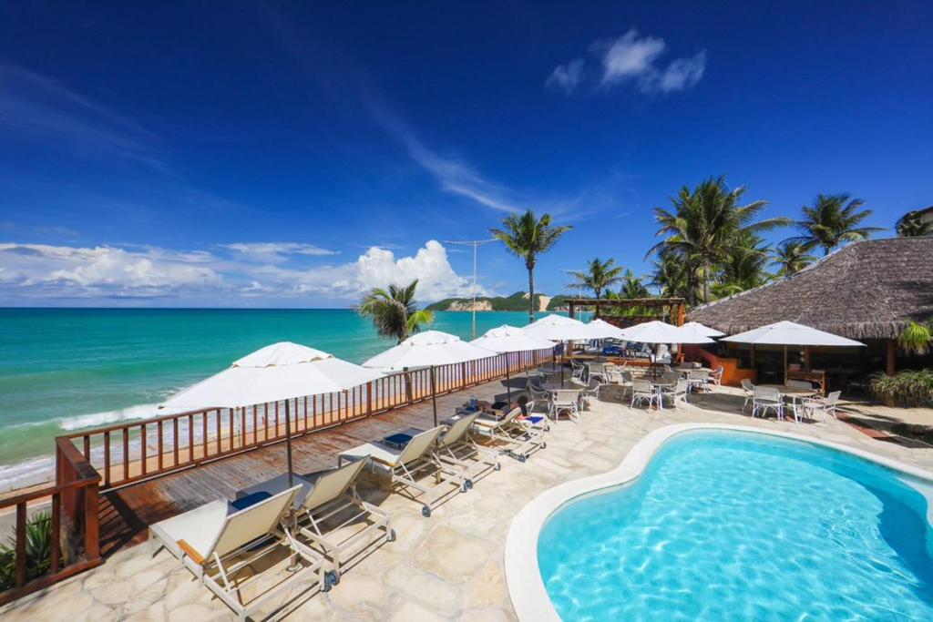 纳塔尔马纳里普莱雅酒店的一个带椅子和遮阳伞的游泳池以及大海