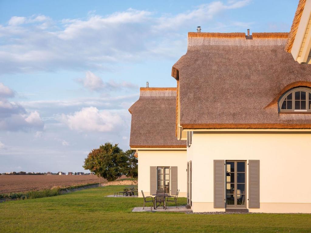 德兰斯克Reetland am Meer - Premium Reetdachvilla mit 2 Schlafzimmern, Sauna und Kamin E04的白色的房子,有棕色的屋顶和田野